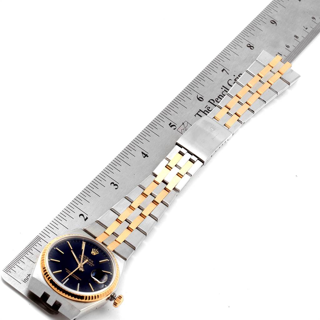 The image shows a Rolex Oysterquartz 17013 Men
s Stainless Steel Black Dial 17013 Men
s Stainless Steel Black Dial watch from an aerial angle, including its dial, bezel, and two-tone bracelet alongside a ruler.