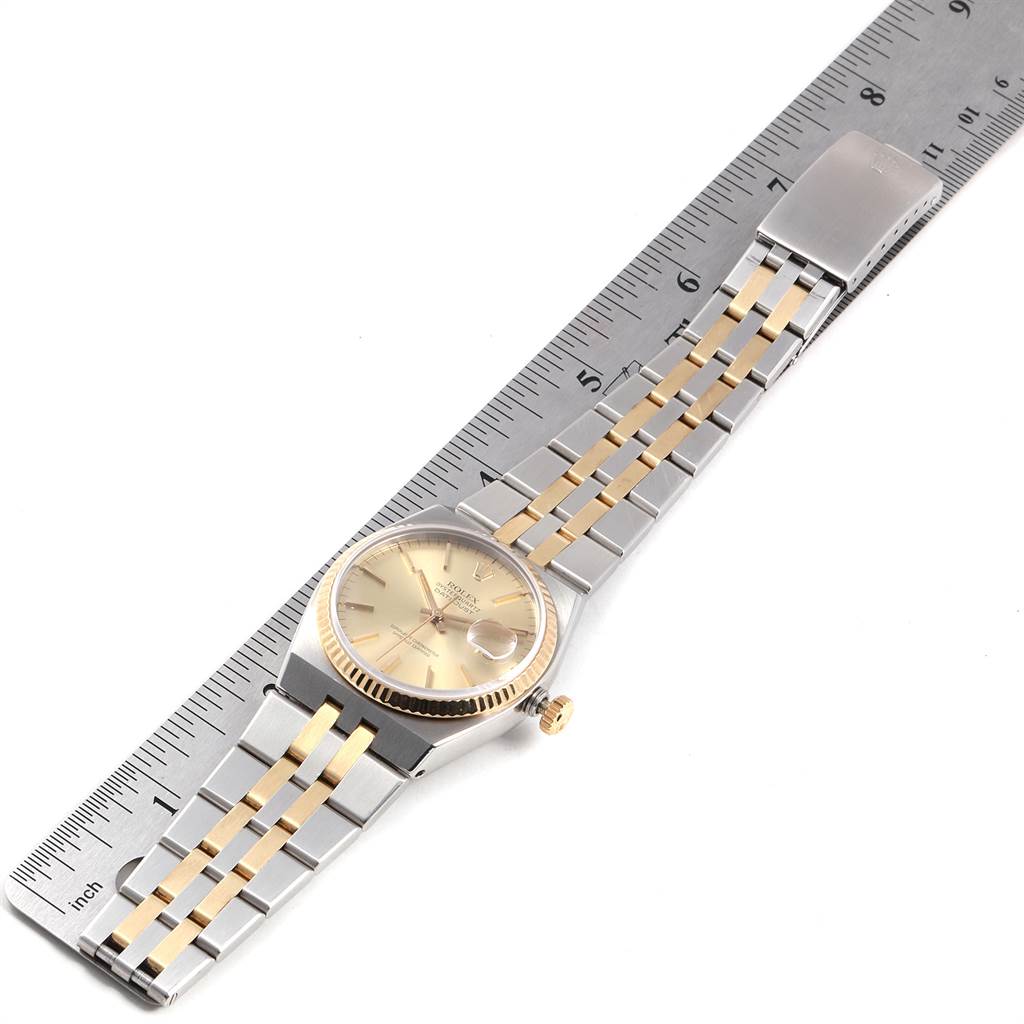 The Rolex Oysterquartz 17013 Men
s Stainless Steel Champagne Dial 17013 Men
s Stainless Steel Champagne Dial watch is shown from a top-down angle, displaying its face, bracelet, and clasp alongside a ruler for scale.