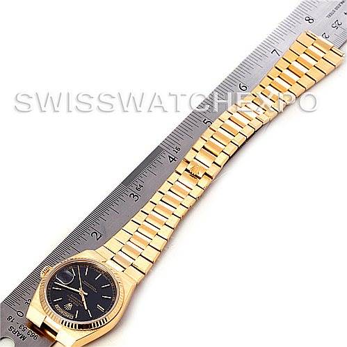 The Rolex President 19018 Men's Yellow Gold Black Dial 19018 Men's Yellow Gold Black Dial model watch is shown from a top-down angle alongside a ruler, displaying its band and face clearly.