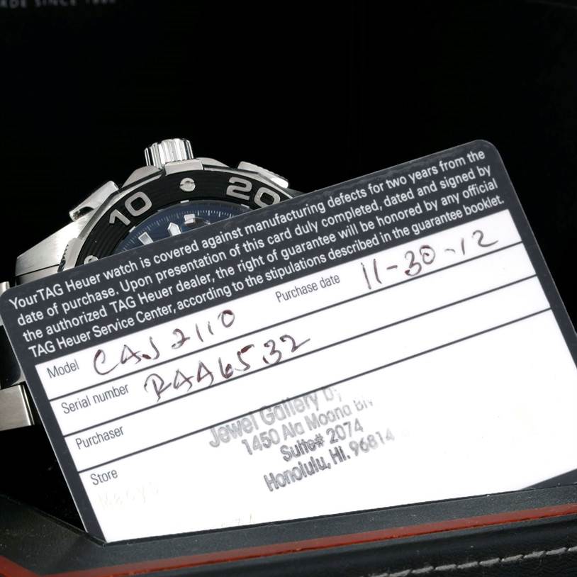 The image shows the bezel, crown, and part of the dial of a Tag Heuer Aquaracer CAJ2110.BA0872 Men's Stainless Steel Black Dial CAJ2110.BA0872 Men's Stainless Steel Black Dial watch, along with its warranty card.