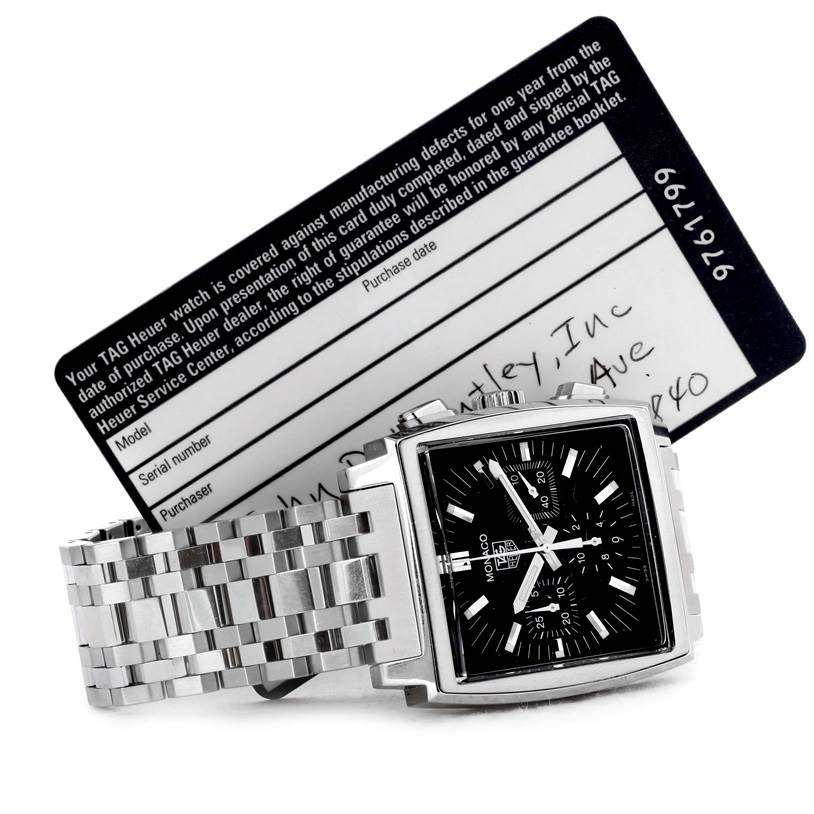 The image shows a Tag Heuer Monaco CW2111.BA0780 Men's Stainless Steel Black Dial CW2111.BA0780 Men's Stainless Steel Black Dial watch at an angle displaying its face and bracelet, with a warranty card in the background.