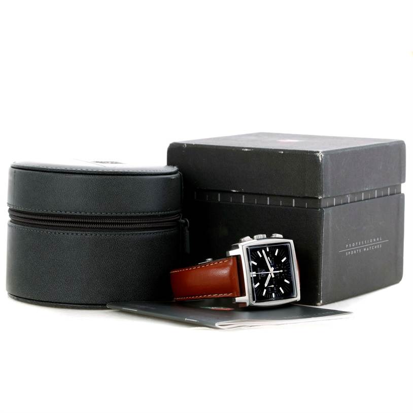 The image shows a Tag Heuer Monaco CW2111 Men's Stainless Steel Black Dial CW2111 Men's Stainless Steel Black Dial watch with a black dial, brown strap, and its accessories, including a black cylindrical case and a rectangular box.