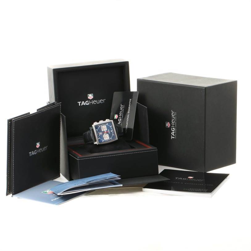 The Tag Heuer Monaco CW2113 Men
s Stainless Steel Blue Dial CW2113 Men
s Stainless Steel Blue Dial watch and its accessories are displayed in their box with manuals and warranty cards surrounding them.