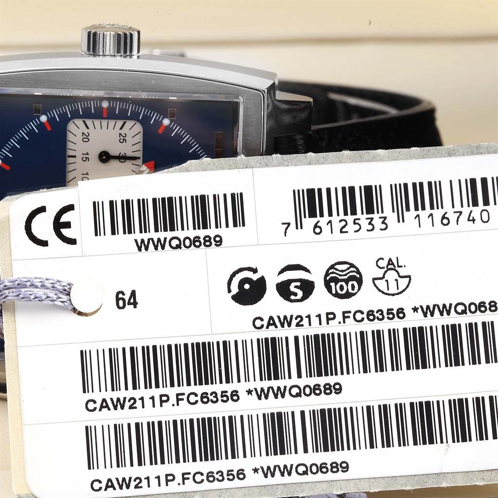 The image shows a partial front view of the Tag Heuer Monaco CAW211P Men's Stainless Steel Blue Dial CAW211P Men's Stainless Steel Blue Dial watch, accompanied by a tag with model and serial numbers.