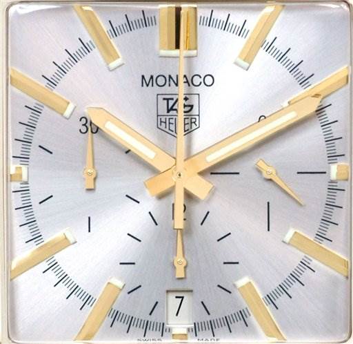 The image shows a close-up of the Tag Heuer Monaco CW5140 Men's Yellow Gold Silver Dial CW5140 Men's Yellow Gold Silver Dial watch face, highlighting the hands, markers, logo, and date window.