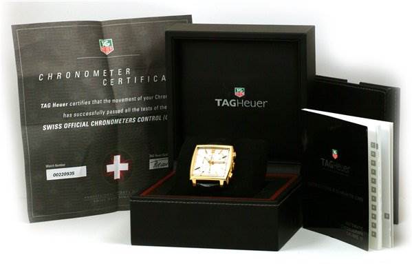 The image shows a Tag Heuer Monaco CW5140 Men's Yellow Gold Silver Dial CW5140 Men's Yellow Gold Silver Dial model watch in its box, along with its chronometer certificate and instructional booklets.