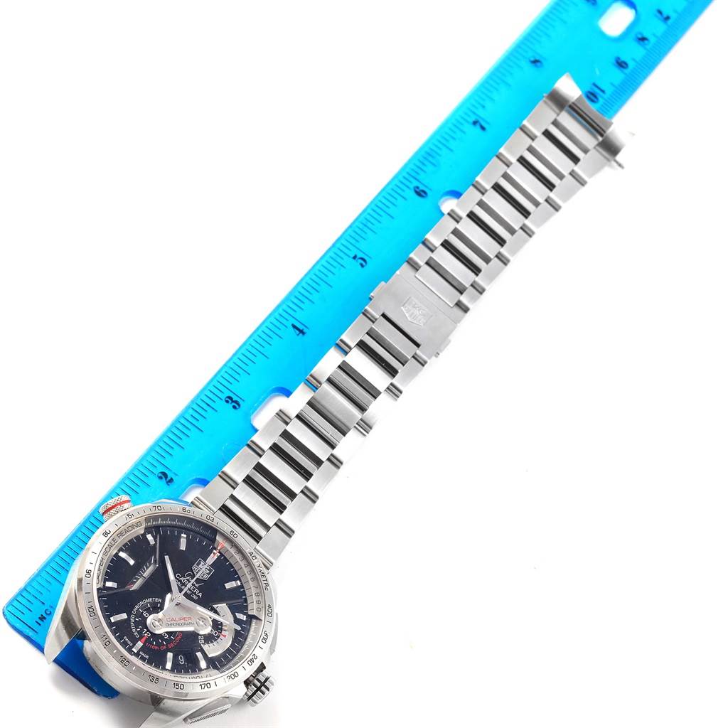 The image shows a Tag Heuer Carrera CAV5115 Men's Stainless Steel Black Dial CAV5115 Men's Stainless Steel Black Dial watch face and metal strap placed next to a blue ruler, viewed from an overhead angle.