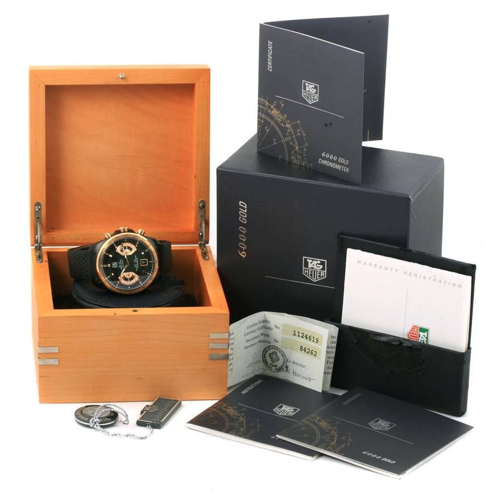 The Tag Heuer Carrera CAV518E.FT6016 Men's Rose Gold Black Dial CAV518E.FT6016 Men's Rose Gold Black Dial watch is displayed in an open wooden box, with its accessories including booklets and tags surrounding it.