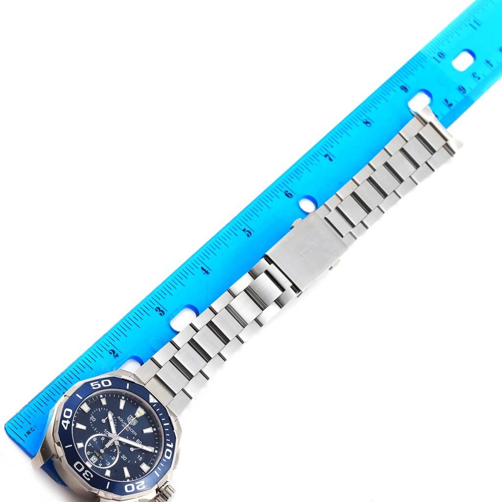 The image shows a Tag Heuer Aquaracer CAY111B.BA0927 Men's Stainless Steel Blue Dial CAY111B.BA0927 Men's Stainless Steel Blue Dial watch laid alongside a blue ruler, focusing on the watch face and metal bracelet.