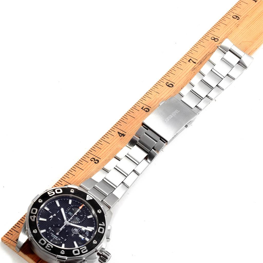 The image shows a Tag Heuer Aquaracer CAJ2110.BA0872 Men's Stainless Steel Black Dial CAJ2110.BA0872 Men's Stainless Steel Black Dial watch laid alongside a ruler from an angled top-down perspective, showcasing the watch face and metal bracelet.