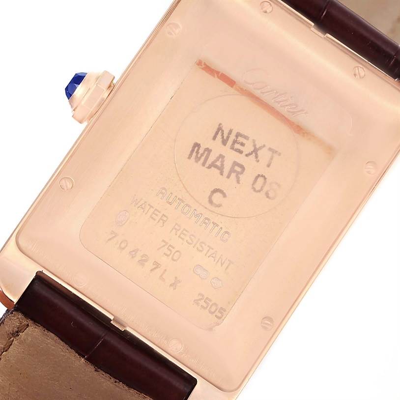 The image shows the back of the Cartier Tank Americaine W2609156 Rose Gold Silver Dial W2609156 Rose Gold Silver Dial watch, with visible engravings and a blue gemstone on the crown.