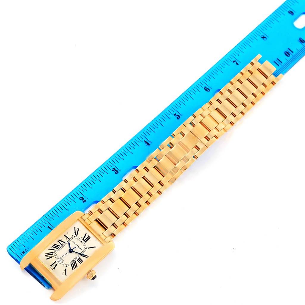 The image shows a Cartier Tank Americaine W26031K2 Men
s Yellow Gold Silver Dial W26031K2 Men
s Yellow Gold Silver Dial watch laid flat next to a ruler for measurement.