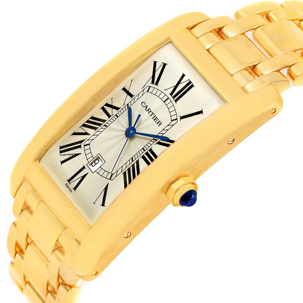 The image shows a close-up angle of a Cartier Tank Americaine W26031K2 Men
s Yellow Gold Silver Dial W26031K2 Men
s Yellow Gold Silver Dial watch, highlighting its gold case, bracelet, and crown with a blue cabochon.