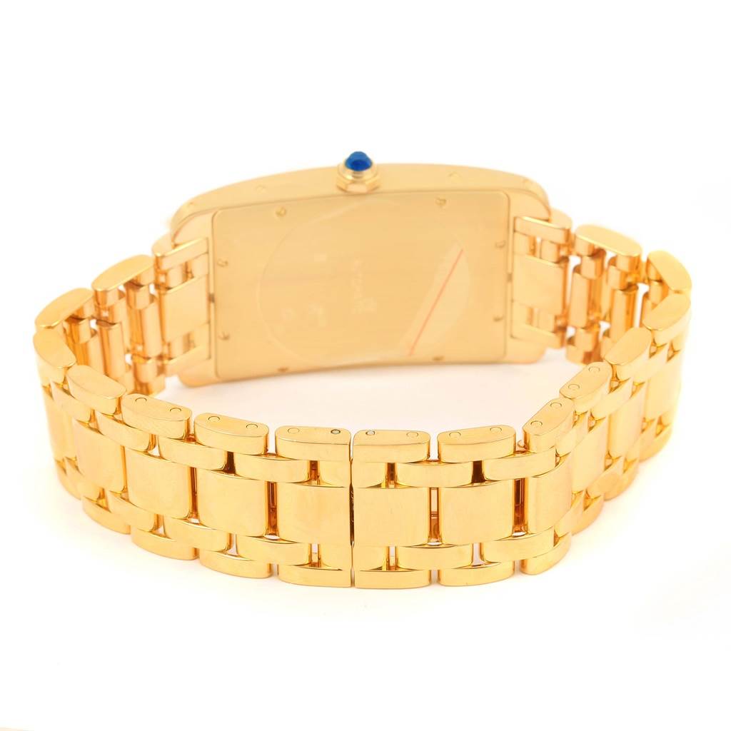The image shows the back view of a Cartier Tank Americaine W26031K2 Men
s Yellow Gold Silver Dial W26031K2 Men
s Yellow Gold Silver Dial watch, highlighting its gold bracelet and case with a blue sapphire crown.