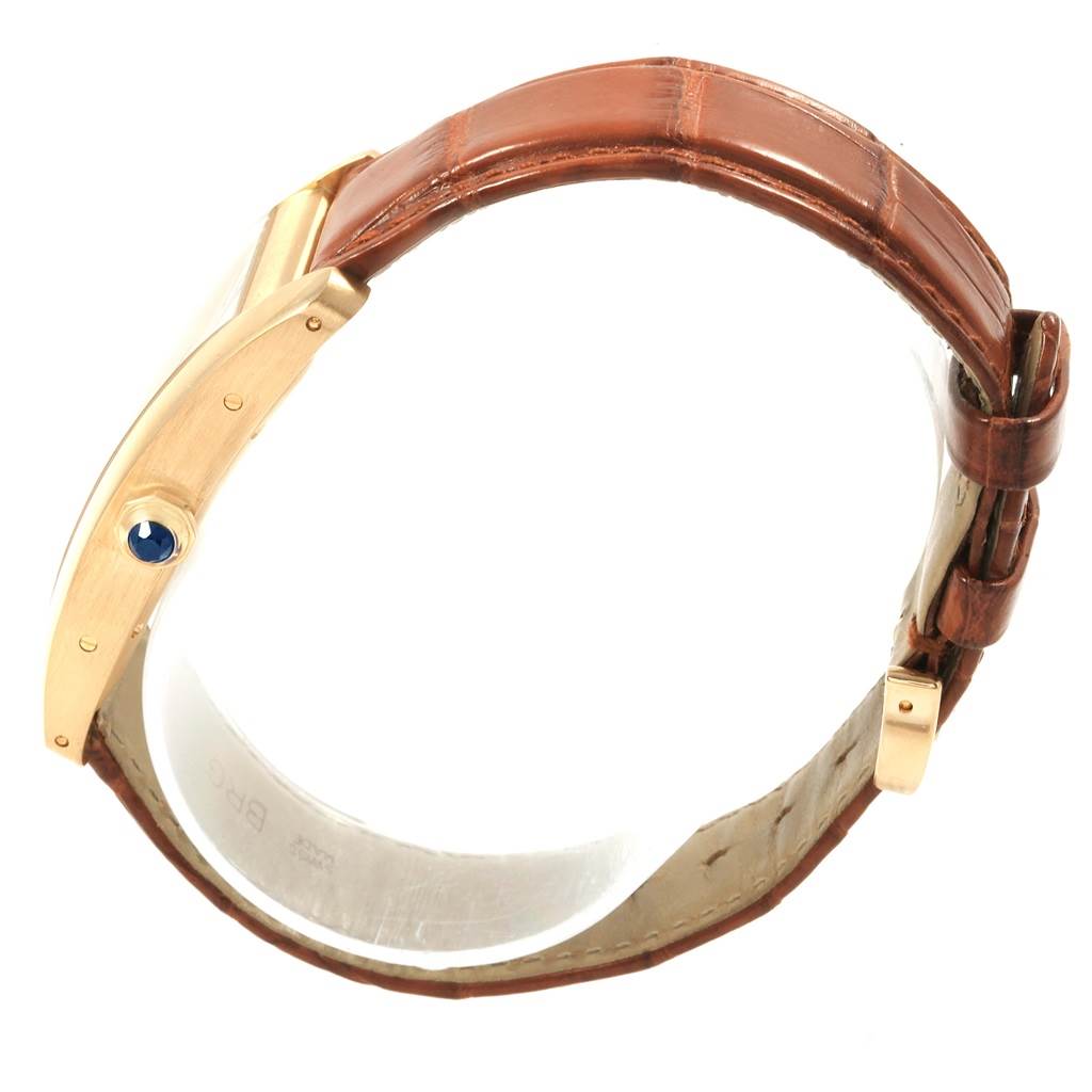 The image shows a side view of the Cartier Tank Américaine watch, highlighting the gold case, brown leather strap, and sapphire cabochon crown.