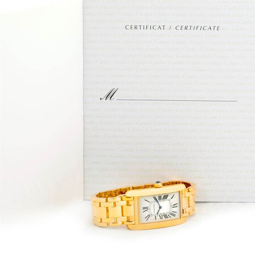 The image shows the Cartier Tank Americaine 1735 Men
s Yellow Gold Silver Dial 1735 Men
s Yellow Gold Silver Dial watch situated horizontally, along with its certificate in the background.