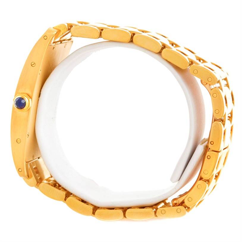 This image shows a side view of the Cartier Tank Americaine 1735 Men
s Yellow Gold Silver Dial 1735 Men
s Yellow Gold Silver Dial watch, highlighting the gold bracelet and blue cabochon crown.