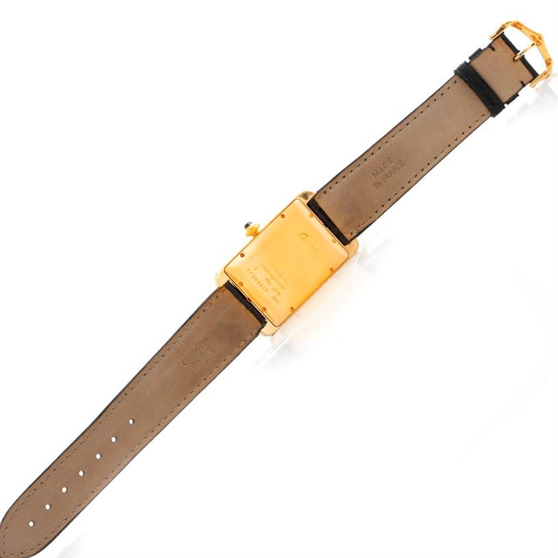 The image shows the backside of a Cartier Tank Americaine W2603156 Men's Yellow Gold Silver Dial W2603156 Men's Yellow Gold Silver Dial watch, including its case back, leather strap, and clasp.