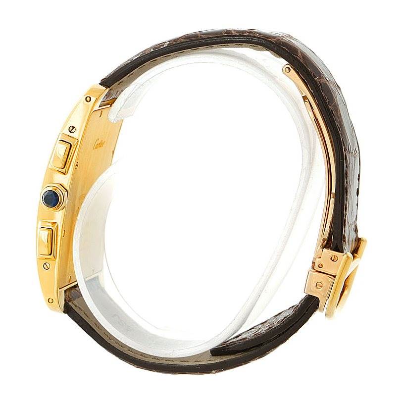 The image shows a Cartier Tank Americaine W2605856 Men's Yellow Gold Silver Dial W2605856 Men's Yellow Gold Silver Dial watch from a side angle, highlighting its case, crown, and brown leather strap.