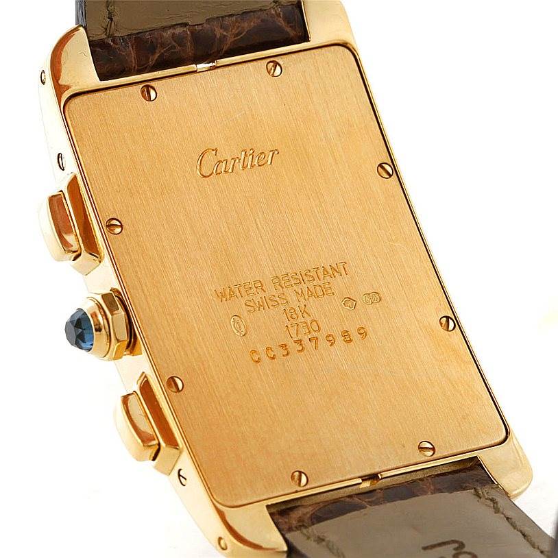 The image shows the backside of a Cartier Tank Americaine W2605856 Men's Yellow Gold Silver Dial W2605856 Men's Yellow Gold Silver Dial watch, displaying the gold case, inscriptions, and part of the leather strap.