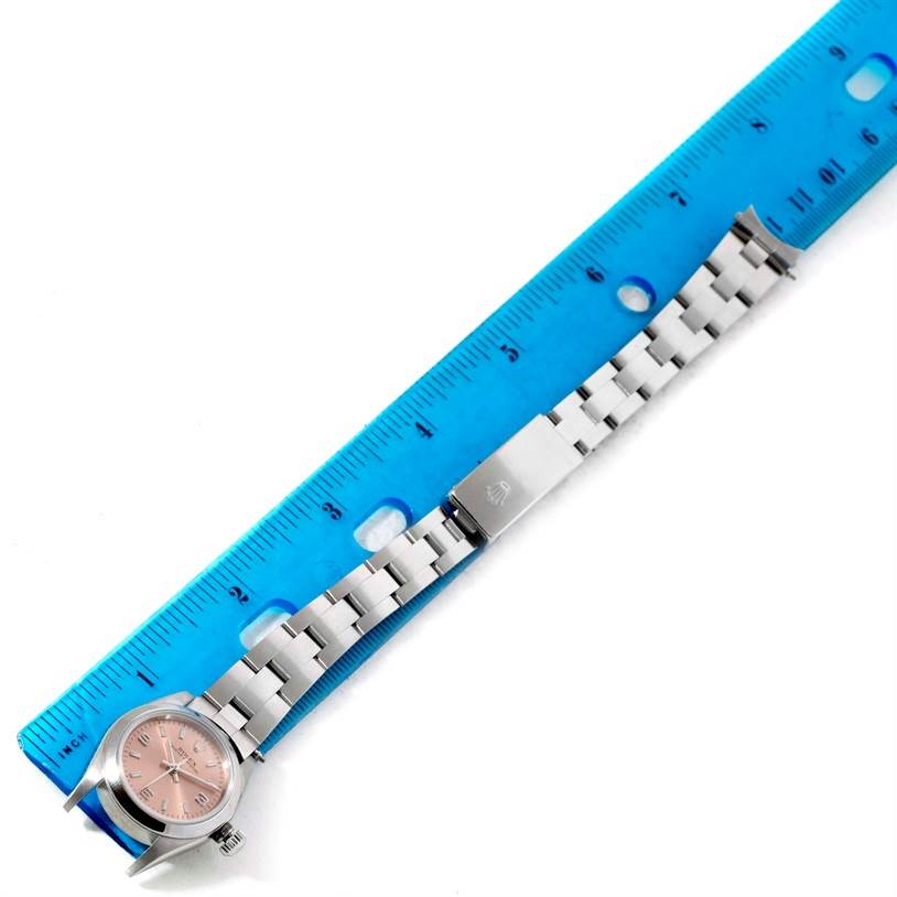 The Rolex Oyster Perpetual 76080 Women's Stainless Steel Pink Dial 76080 Women's Stainless Steel Pink Dial watch is displayed flat with a blue ruler next to it, showing the case, bracelet, and clasp.
