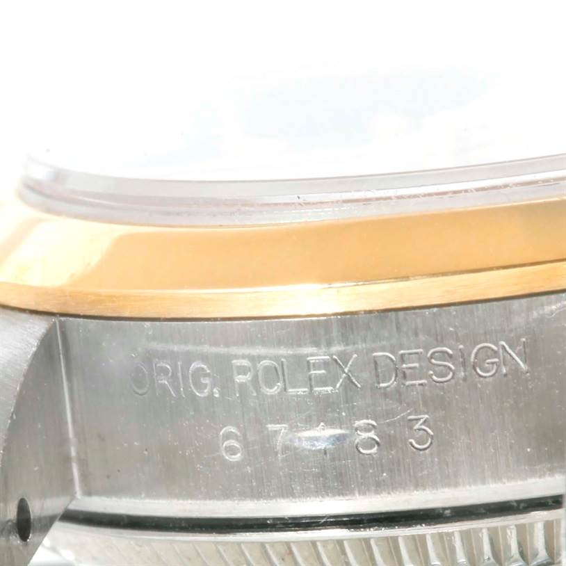 This close-up of a Rolex Oyster Perpetual 67183 Women's Steel and Gold (two tone) Grey Dial 67183 Women's Steel and Gold (two tone) Grey Dial watch shows part of the bezel and case, with engraved text "ORIG. ROLEX DESIGN" and numbers.
