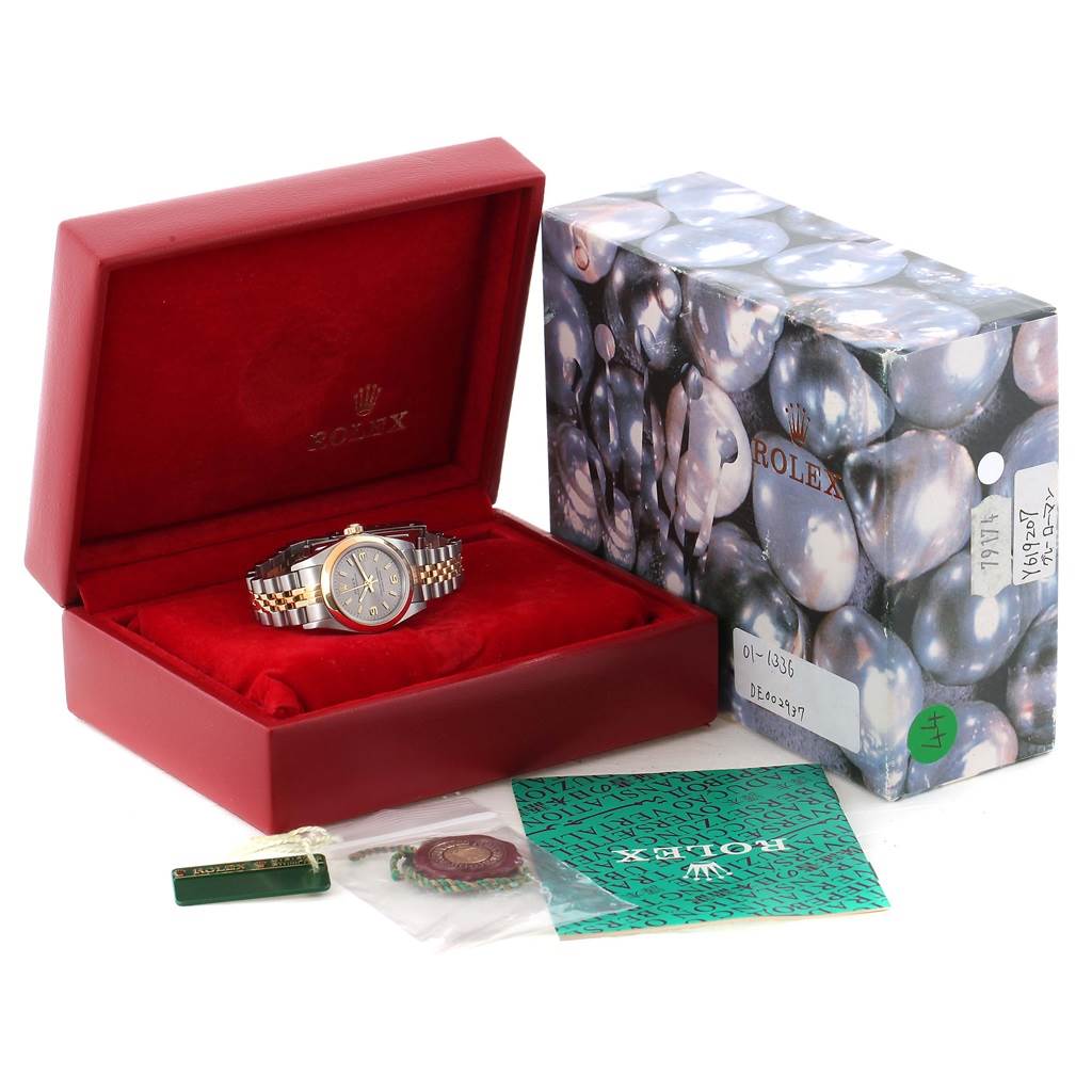 The image shows a Rolex Oyster Perpetual 76183 Women's Steel and Gold (two tone) Grey Dial 76183 Women's Steel and Gold (two tone) Grey Dial watch in a red box, with its packaging and accessories like tags and a booklet.
