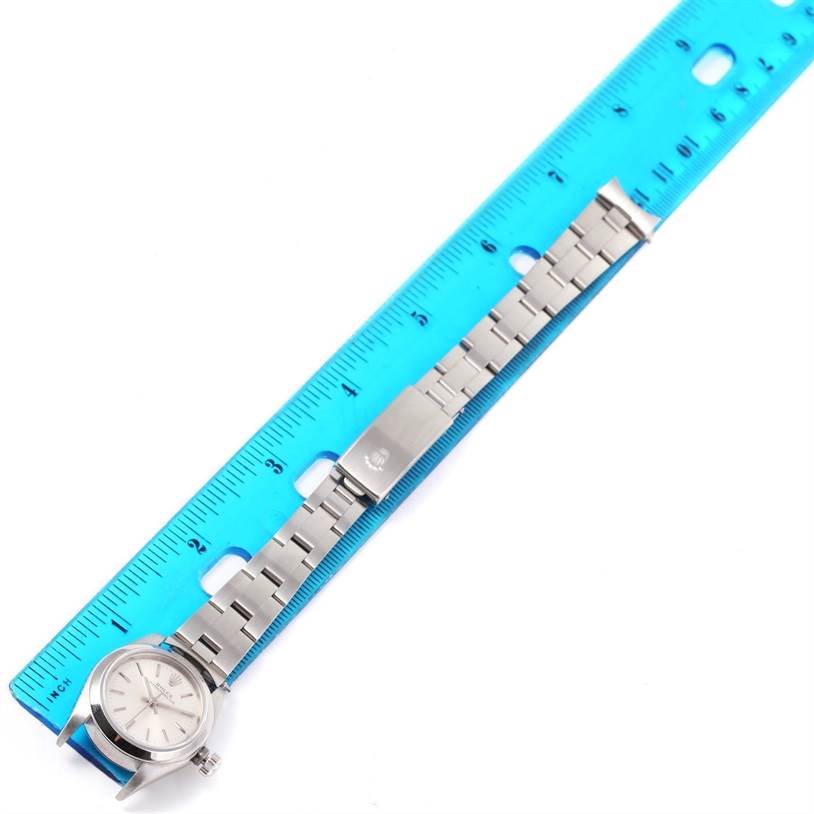 The Rolex Oyster Perpetual 76080 Women
s Stainless Steel Silver Dial 76080 Women
s Stainless Steel Silver Dial watch is shown laying flat with its bracelet aligned beside a blue ruler for measurement.