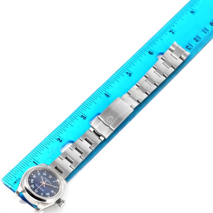The image shows a top-down view of a Rolex Oyster Perpetual 176200 Women's Stainless Steel Blue Dial 176200 Women's Stainless Steel Blue Dial watch next to a blue ruler, focusing on the watch band and clasp.
