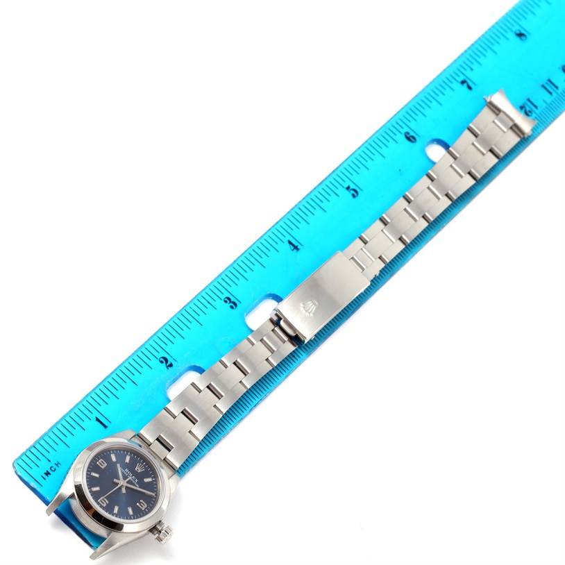 The image shows a Rolex Oyster Perpetual 76080 Women
s Stainless Steel Blue Dial 76080 Women
s Stainless Steel Blue Dial watch with a metal bracelet laid next to a ruler, displaying the watch face and clasp.