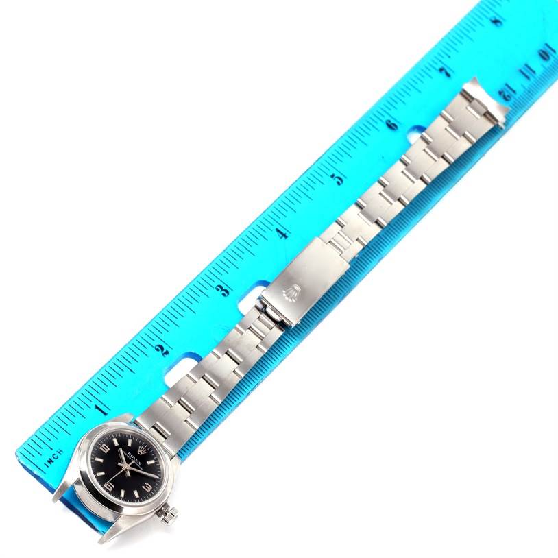 The Rolex Oyster Perpetual 76080 Women's Stainless Steel Black Dial 76080 Women's Stainless Steel Black Dial watch is shown from an overhead angle, displaying its face and band beside a ruler.