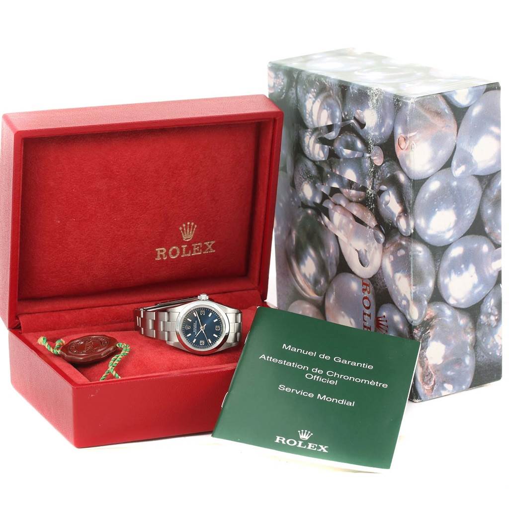 This image shows a Rolex Oyster Perpetual 76080 Women
s Stainless Steel Blue Dial 76080 Women
s Stainless Steel Blue Dial watch in its red box, alongside a green manual and packaging.