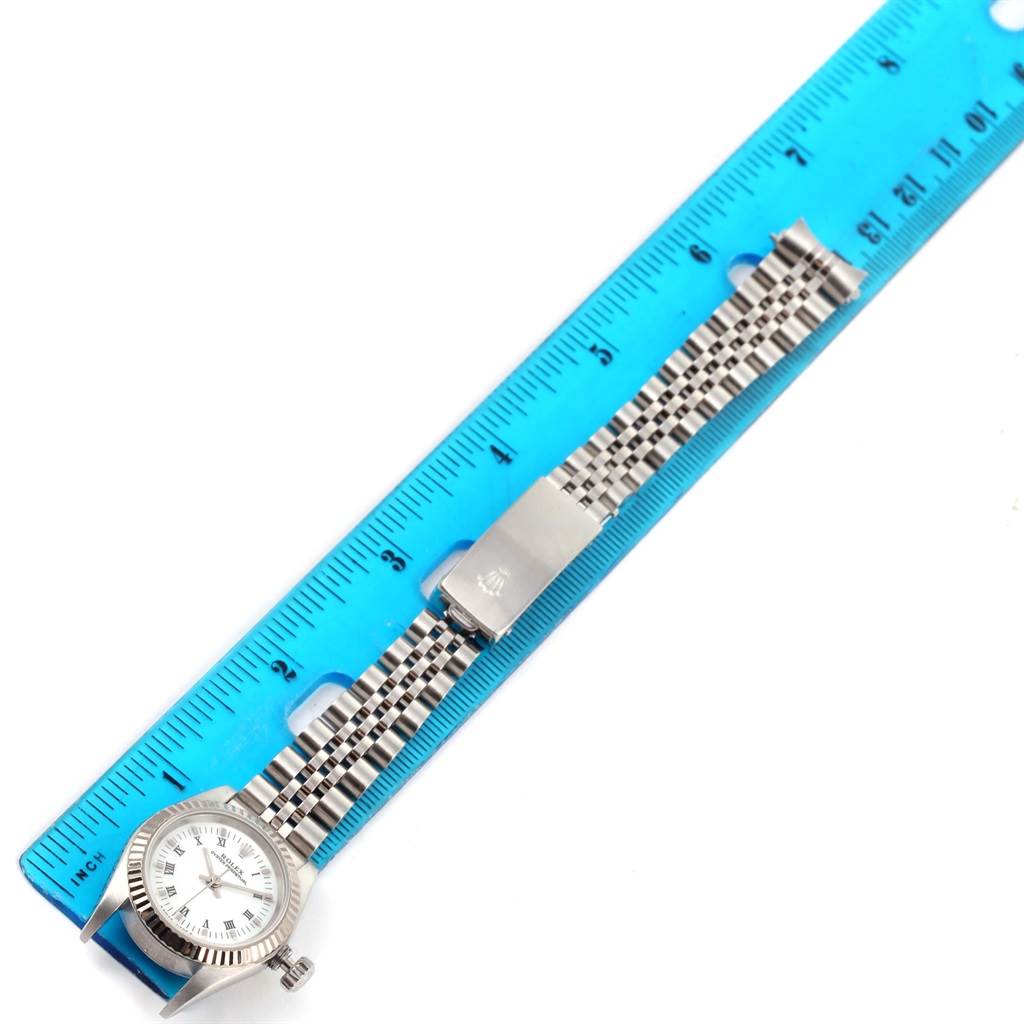 The image shows a Rolex Oyster Perpetual 67194 Women's Stainless Steel White Dial 67194 Women's Stainless Steel White Dial watch laid flat with the bracelet fully extended alongside a blue ruler.