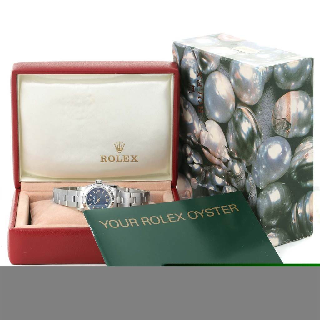 The image shows a Rolex Oyster Perpetual 67180 Men
s Stainless Steel Blue Dial 67180 Men
s Stainless Steel Blue Dial watch from a front angle, along with its opened case, original box, and accompanying booklet.
