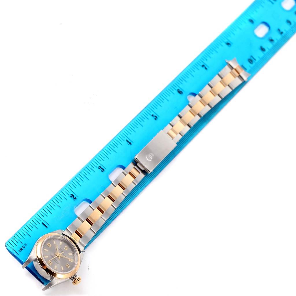 The image shows a Rolex Oyster Perpetual 76183 Women's Steel and Gold (two tone) Grey Dial 76183 Women's Steel and Gold (two tone) Grey Dial watch laid flat next to a ruler, displaying its face and bracelet.