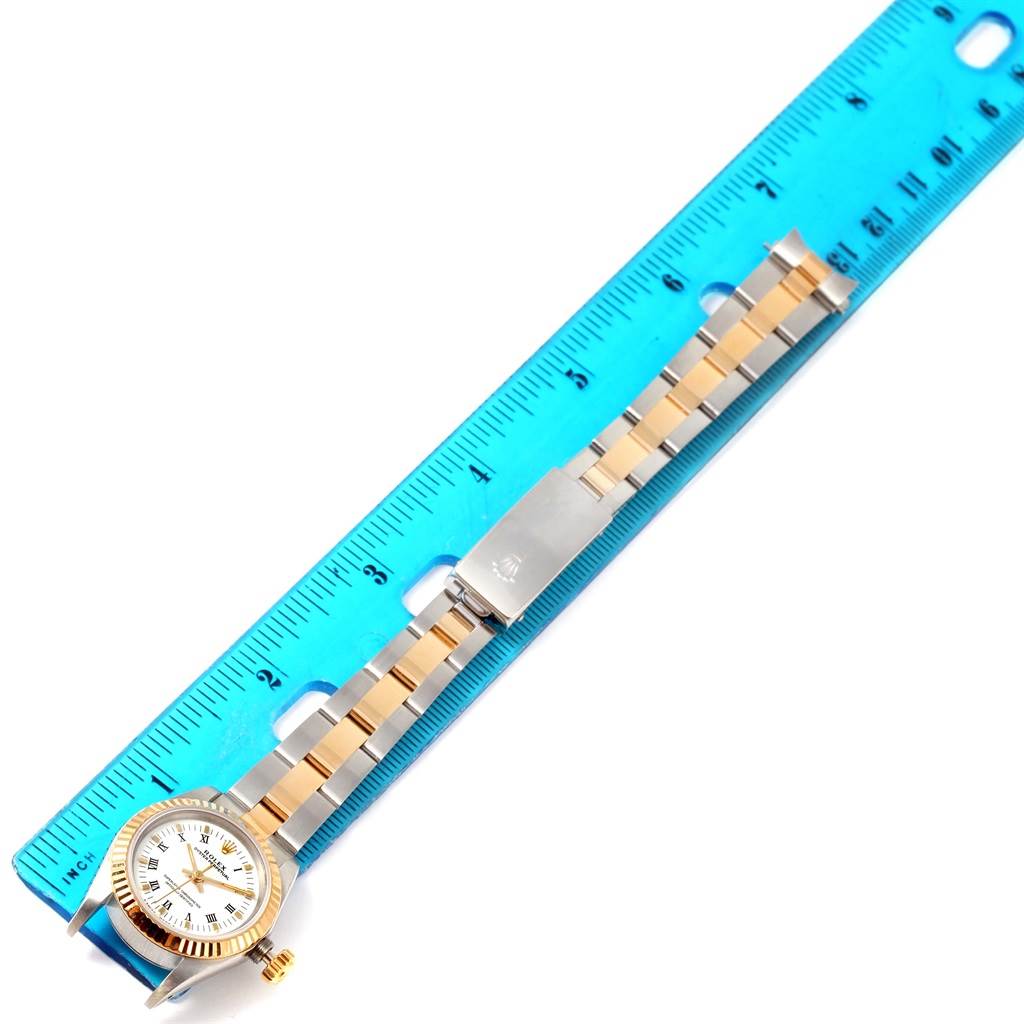 Shown from a top-down angle, this Rolex Oyster Perpetual 67193 Women's Steel and Gold (two tone) White Dial 67193 Women's Steel and Gold (two tone) White Dial watch is displayed alongside a blue ruler for scale.