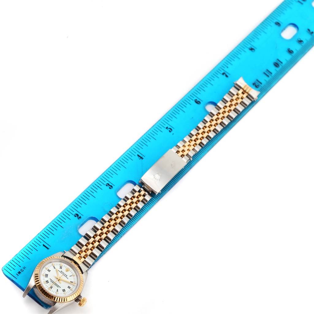 This image shows an overhead view of a Rolex Oyster Perpetual 76193 Women's Steel and Gold (two tone) White Dial 76193 Women's Steel and Gold (two tone) White Dial watch with its bracelet laid alongside a blue ruler.