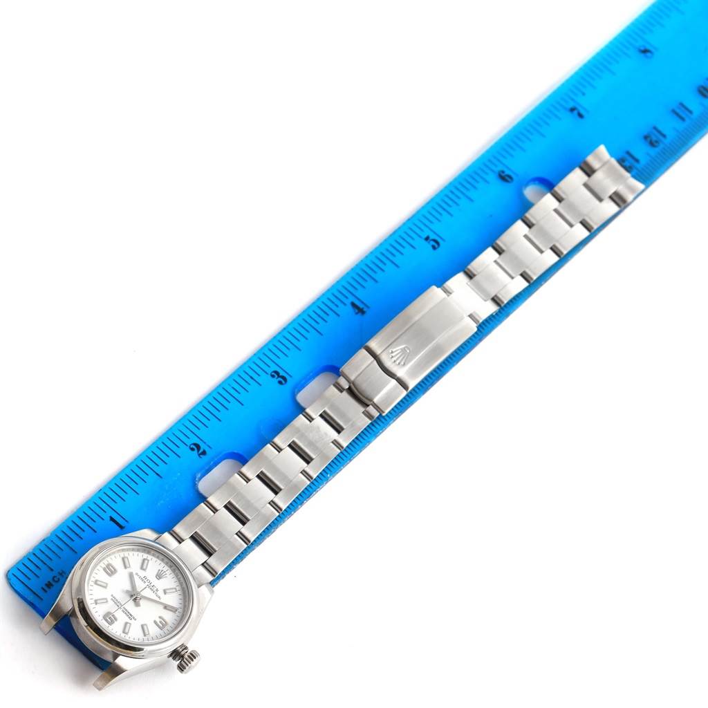 This image shows a Rolex Oyster Perpetual 176200 Women's Stainless Steel White Dial 176200 Women's Stainless Steel White Dial watch laid flat with its metal bracelet beside a blue ruler, displaying its length.