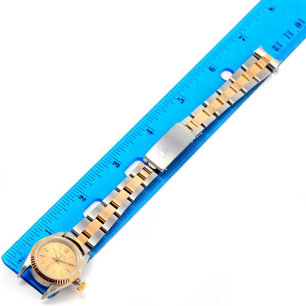 The Rolex Oyster Perpetual 67193 Women's Steel and Gold (two tone) Champagne Dial 67193 Women's Steel and Gold (two tone) Champagne Dial watch is shown flat alongside a ruler, displaying the face, bezel, and entire bracelet.