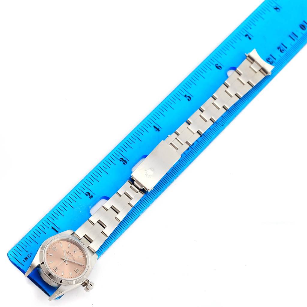 The image shows a Rolex Oyster Perpetual 76030 Women
s Stainless Steel Pink Dial 76030 Women
s Stainless Steel Pink Dial watch laid flat with a blue ruler, displaying its face and entire bracelet.