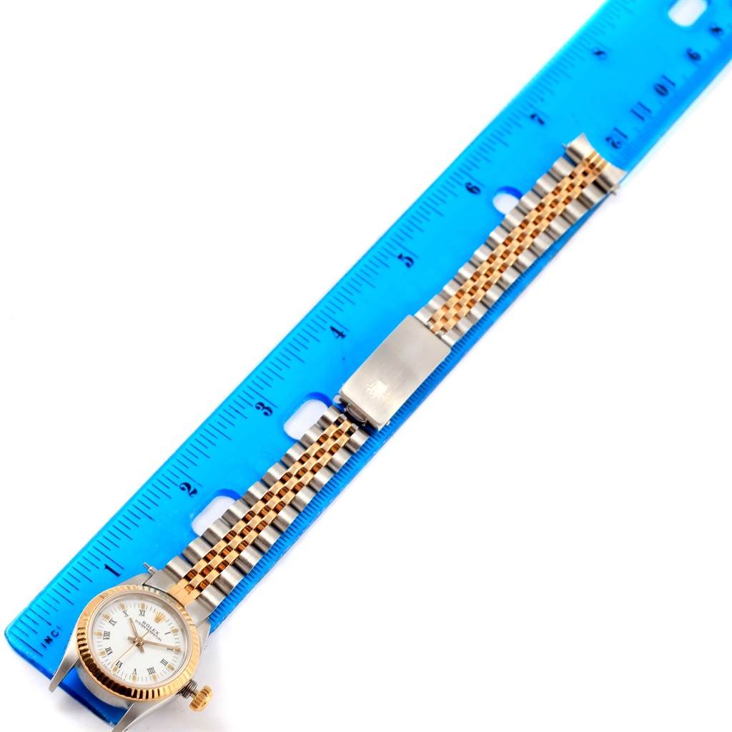 The Oyster Perpetual Rolex watch is displayed flat with the band extended alongside a blue ruler.