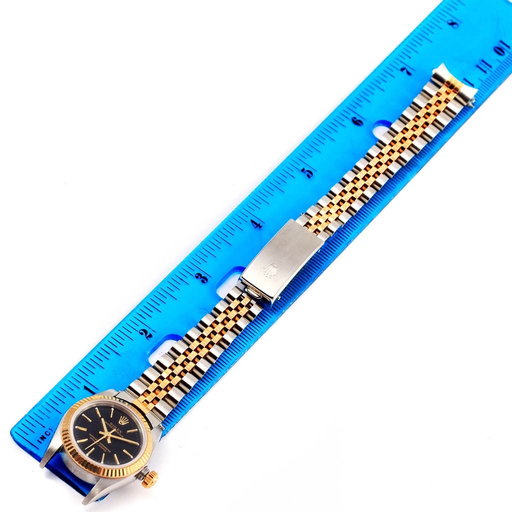 The image shows an Oyster Perpetual Rolex watch with a gold and silver bracelet laid next to a blue ruler.