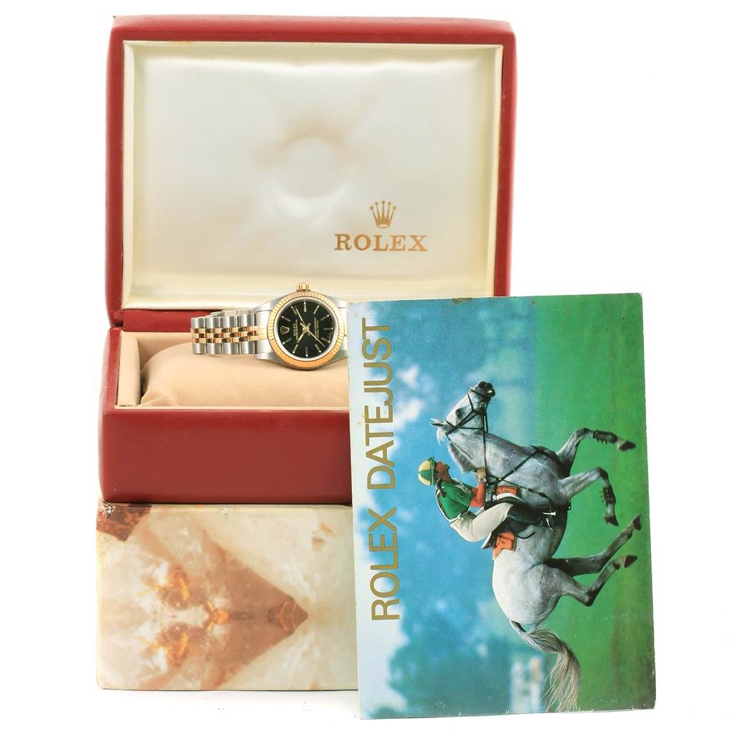 A Rolex Oyster Perpetual 76193 Women's Steel and Gold (two tone) Black Dial 76193 Women's Steel and Gold (two tone) Black Dial watch is shown in its box, with a Rolex Datejust pamphlet in the foreground.