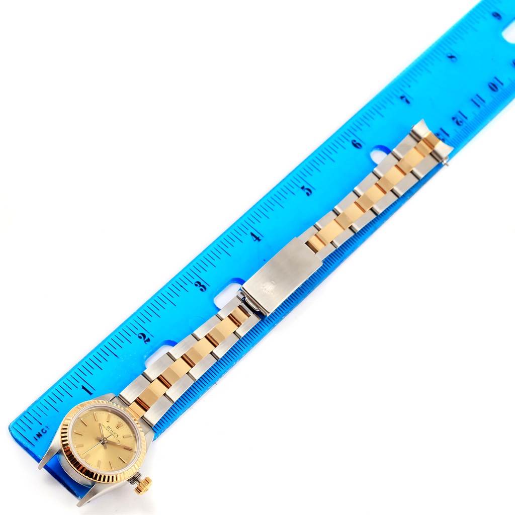 The image shows a Rolex Oyster Perpetual 67193 Women
s Steel and Gold (two tone) Champagne Dial 67193 Women
s Steel and Gold (two tone) Champagne Dial watch laid flat with its bracelet extended next to a blue ruler for measurement.