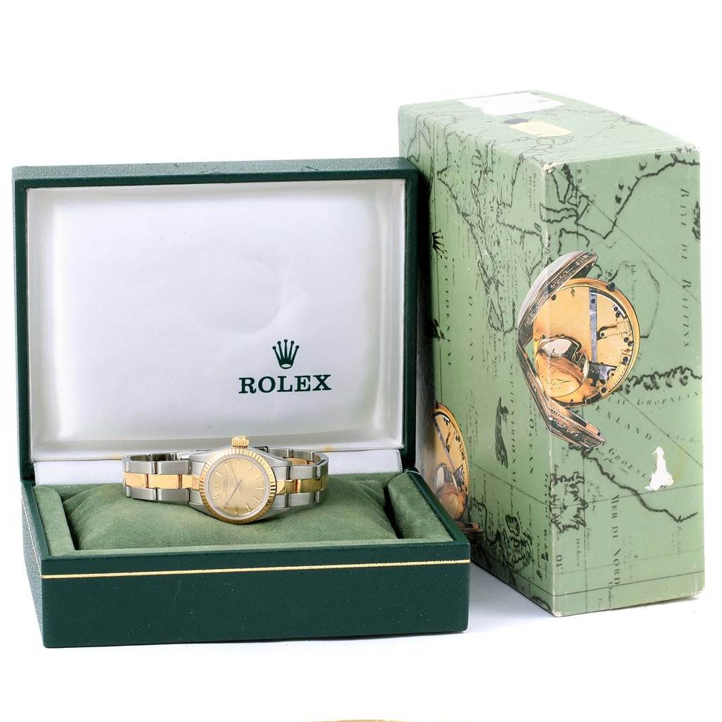 The Rolex Oyster Perpetual 67193 Women
s Steel and Gold (two tone) Champagne Dial 67193 Women
s Steel and Gold (two tone) Champagne Dial watch is displayed inside its green box on a green cushion, with the outer box visible in the background.