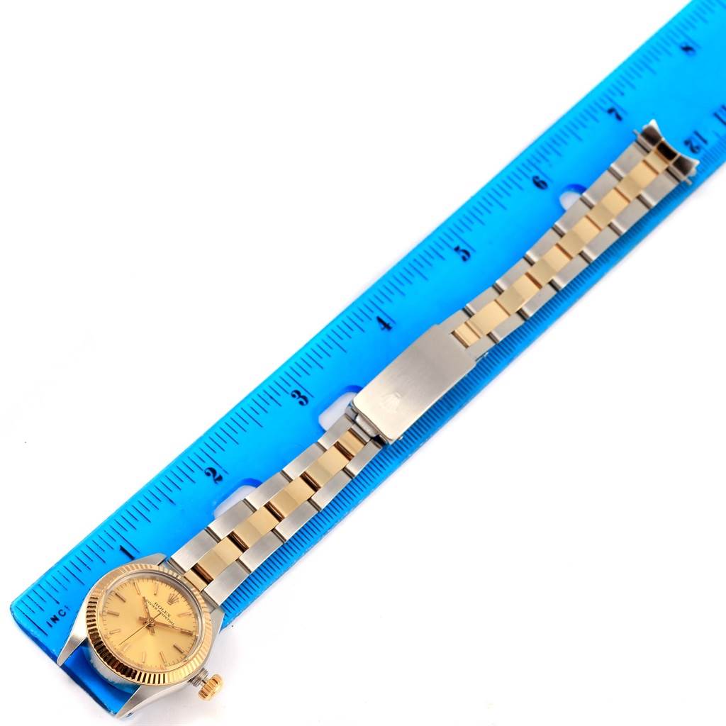 The Rolex Oyster Perpetual 6719 Women's Steel and Gold (two tone) Champagne Dial 6719 Women's Steel and Gold (two tone) Champagne Dial watch is displayed flat alongside a blue ruler, showing the face and entire metal band.