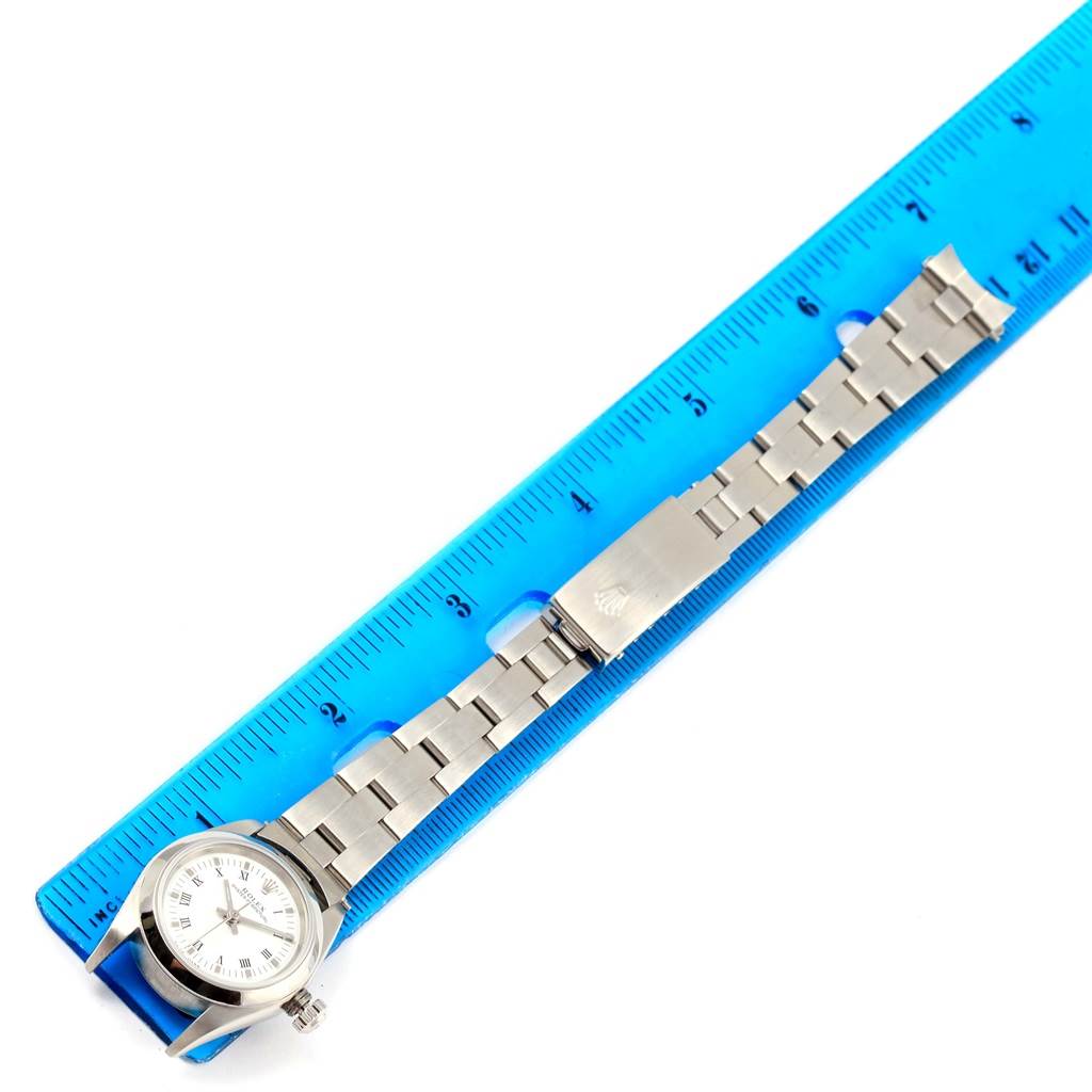 The Rolex Oyster Perpetual 76080 Women
s Stainless Steel White Dial 76080 Women
s Stainless Steel White Dial watch is shown from a top-down angle with the bracelet extended alongside a blue ruler.