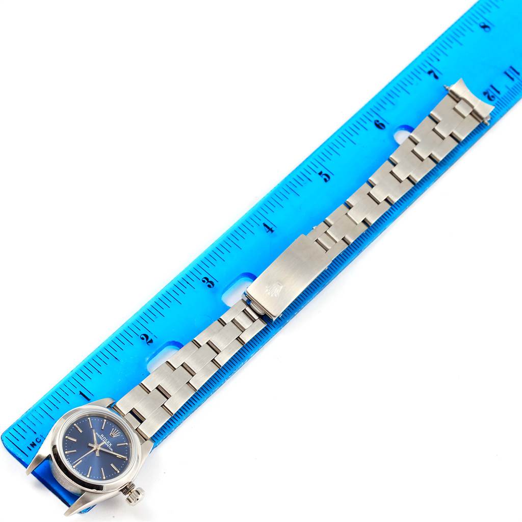 This image shows the Rolex Oyster Perpetual 67180 Women
s Stainless Steel Blue Dial 67180 Women
s Stainless Steel Blue Dial watch laid flat next to a ruler, displaying the watch case and bracelet.