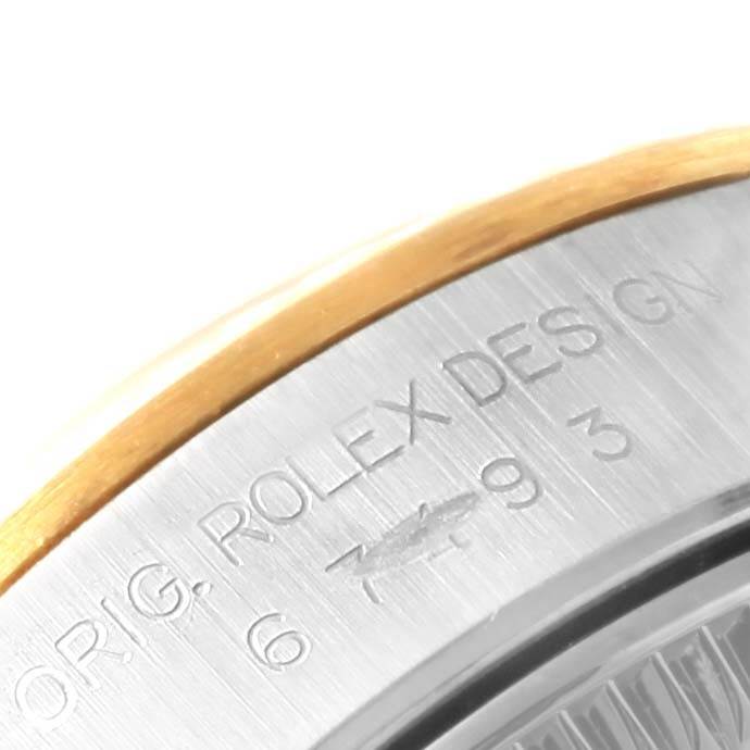 This close-up image shows part of the bezel and casing with "ROLEX DESIGN" engraving of the Rolex Oyster Perpetual 67193 Women's Steel and Gold (two tone) Black Dial 67193 Women's Steel and Gold (two tone) Black Dial watch.