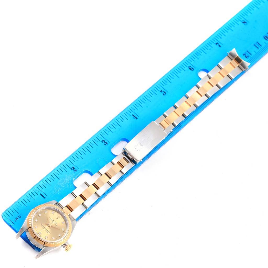 The image shows a top view of a Rolex Oyster Perpetual 76243 Women's Steel and Gold (two tone) Champagne Dial 76243 Women's Steel and Gold (two tone) Champagne Dial watch with a gold and silver band next to a blue ruler for scale.